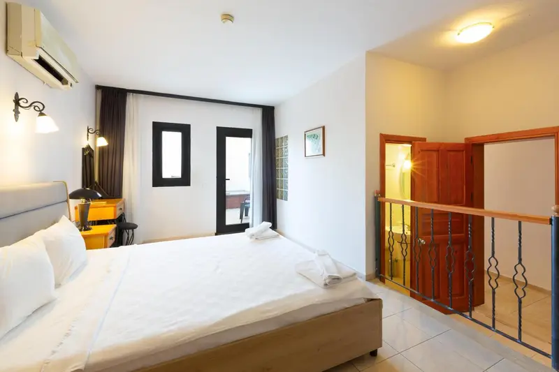 Une chambre lumineuse avec un lit blanc et un accès à une autre pièce.