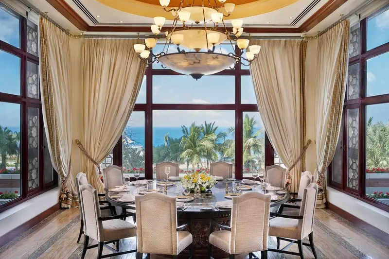 Une table ronde est dressée dans une salle lumineuse avec de grandes fenêtres donnant sur la mer.