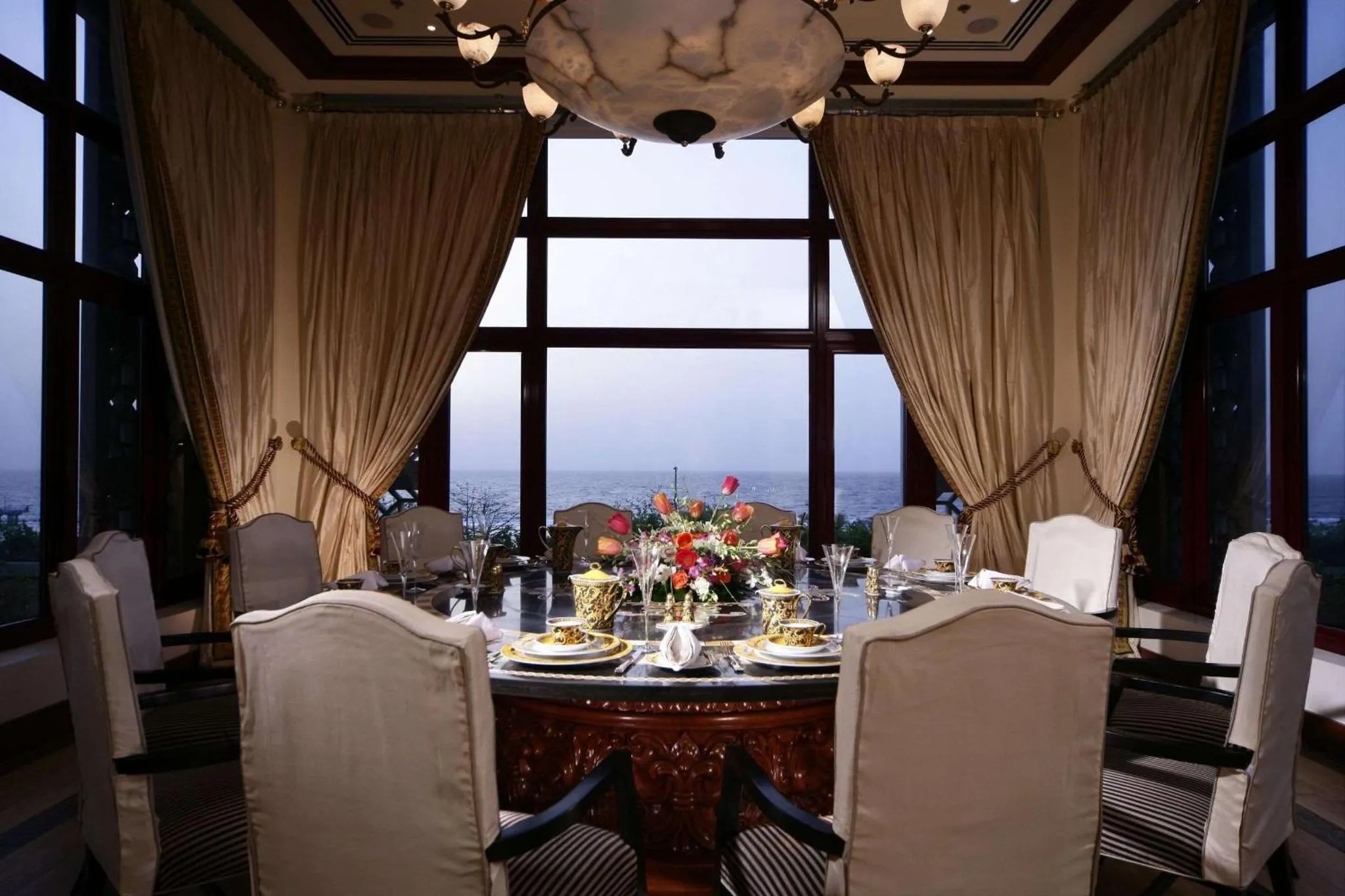 Une table ronde est dressée devant une grande baie vitrée donnant sur la mer.