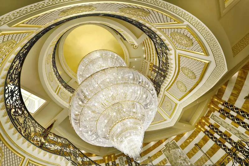 Un escalier en colimaçon orné d'un lustre scintillant illumine un intérieur luxueux.