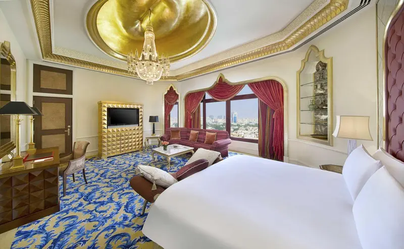 Une chambre spacieuse avec un lit king-size et un canapé rouge, décorée de motifs dorés et de rideaux sombres.