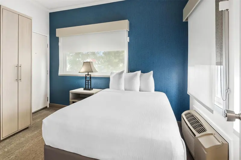 Une chambre lumineuse avec un grand lit blanc et une armoire.
