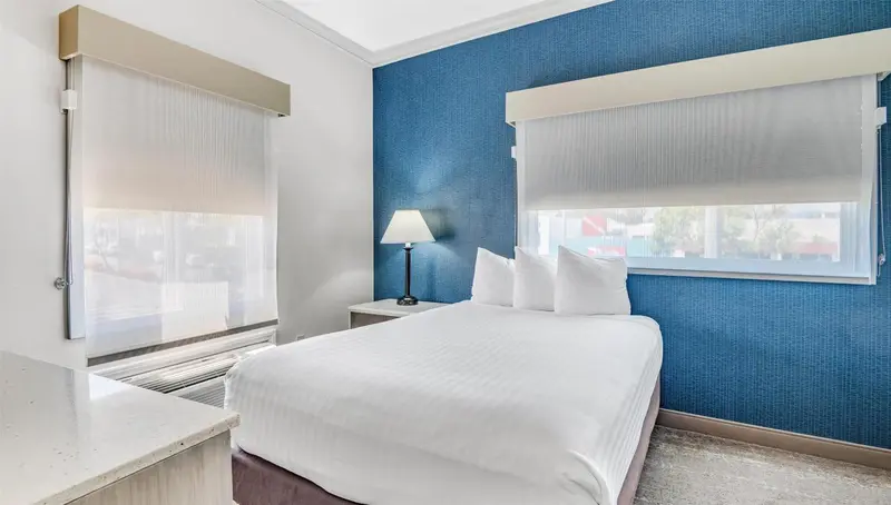 Une chambre lumineuse avec un lit blanc et deux fenêtres.