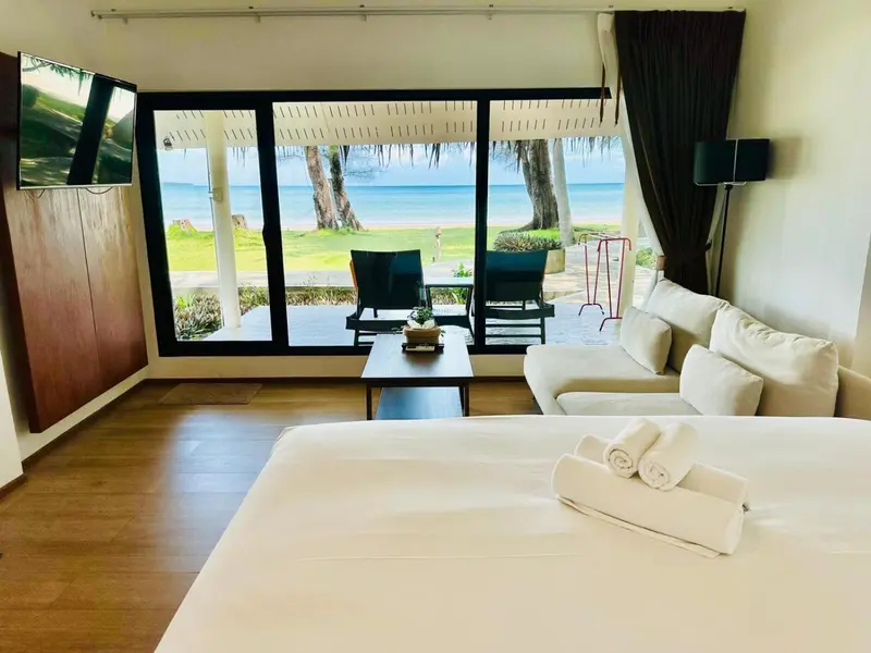 Une chambre lumineuse avec un grand lit et un canapé face à une baie vitrée donnant sur la mer.