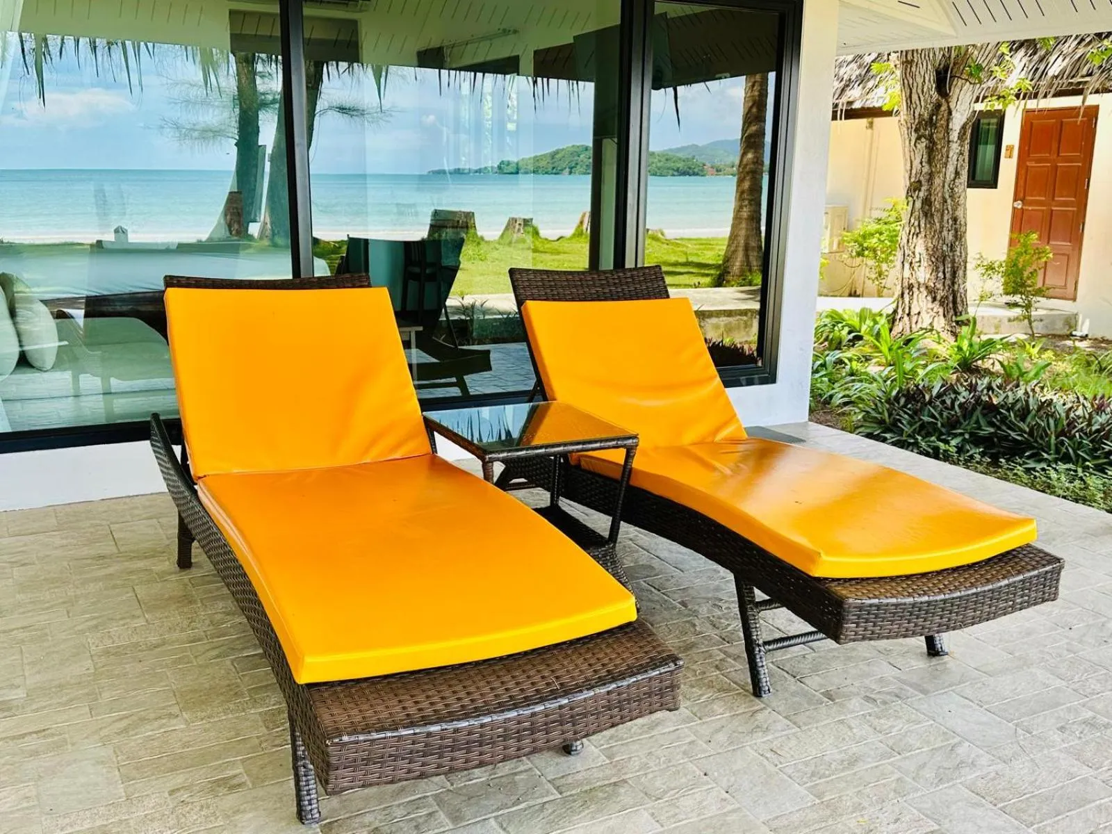 Deux transats orange reposent sur une terrasse carrelée face à la mer.