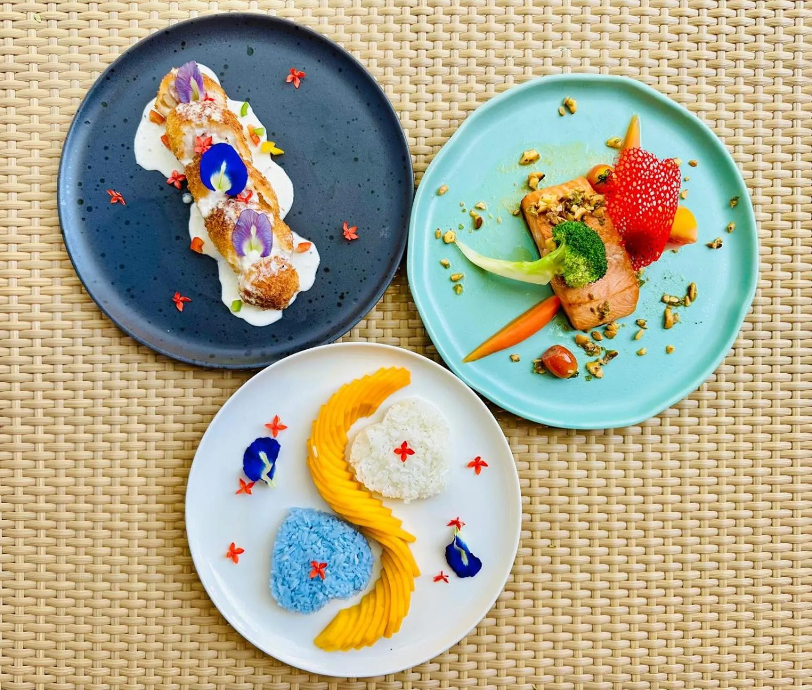 Trois assiettes colorées présentent des plats décorés de fleurs et de fruits.
