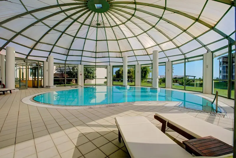 Une piscine intérieure lumineuse avec des transats et une grande baie vitrée.