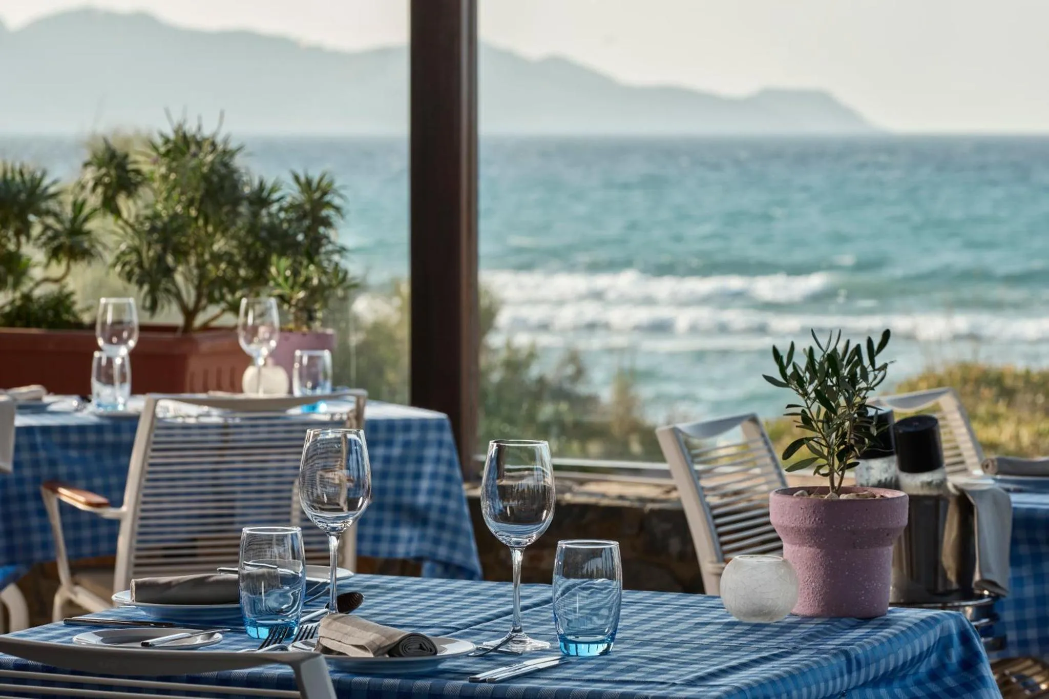 Une table est dressée avec de la vaisselle et des verres devant une vue sur la mer.