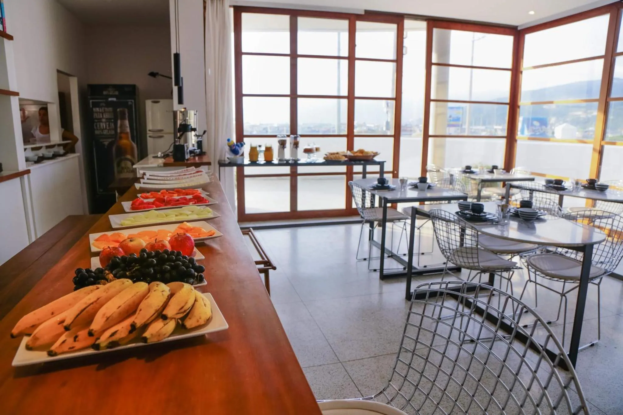 Un buffet propose des fruits frais et des viennoiseries dans une salle lumineuse avec de grandes baies vitrées.