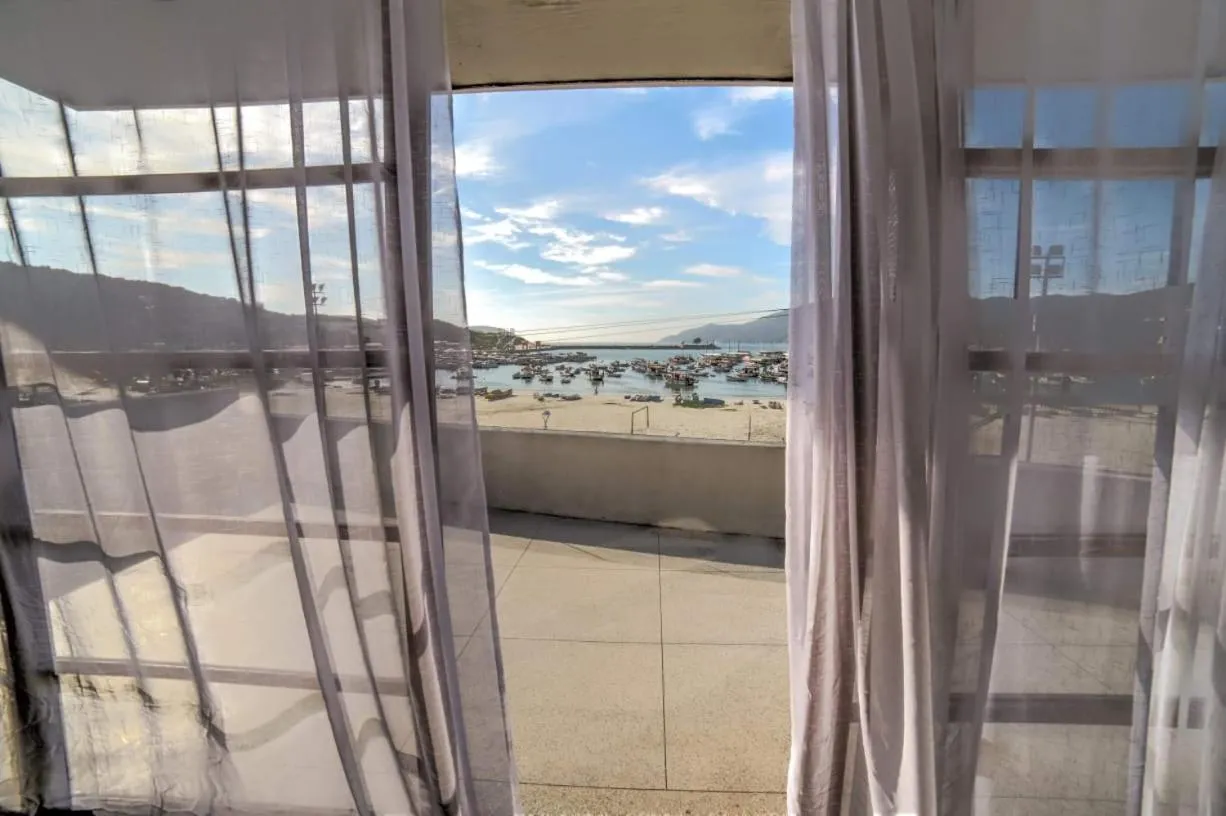 Vue sur une plage et des bateaux depuis un balcon ombragé.