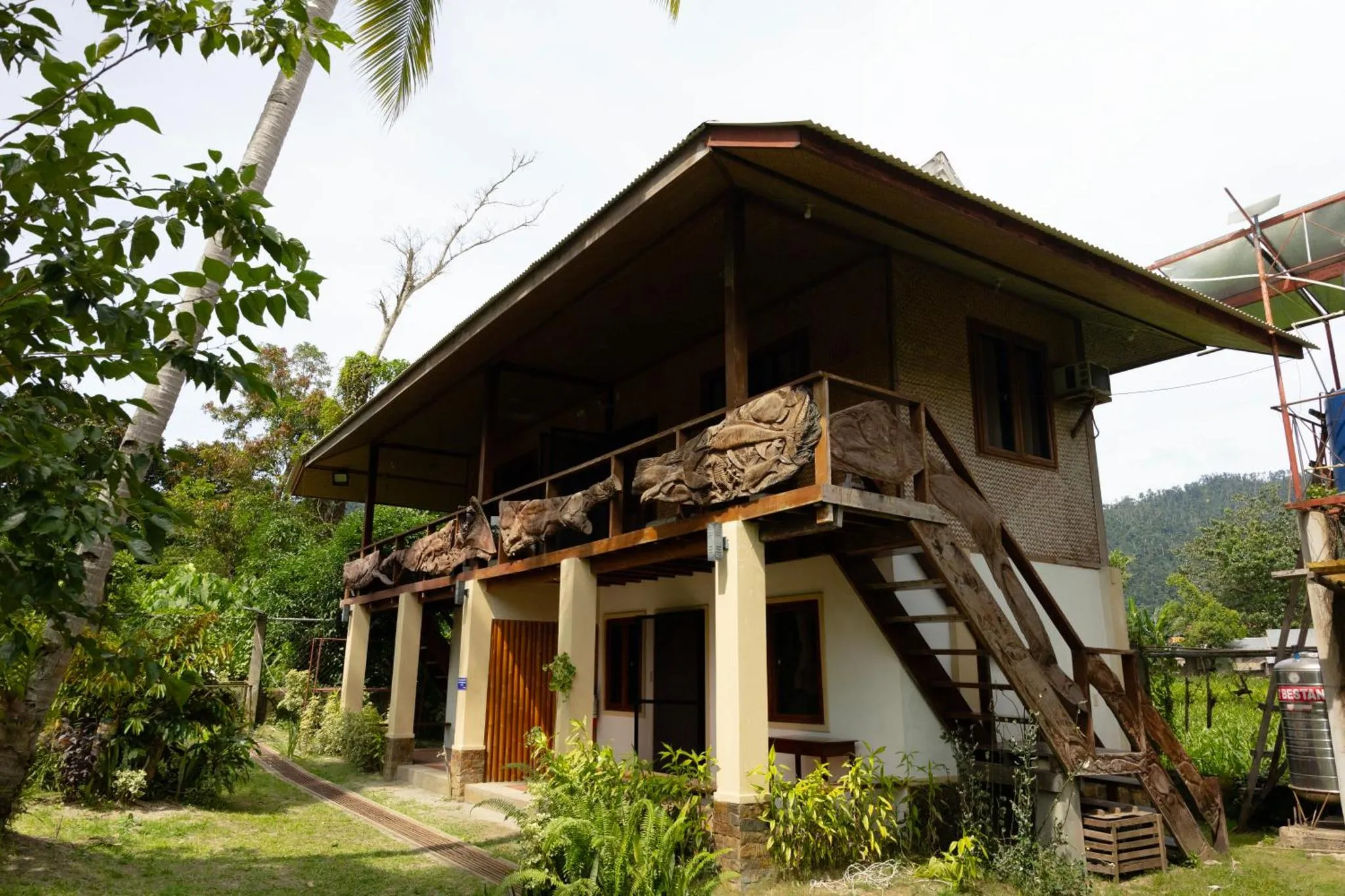 Bâtiment à deux étages avec balcon et végétation luxuriante.