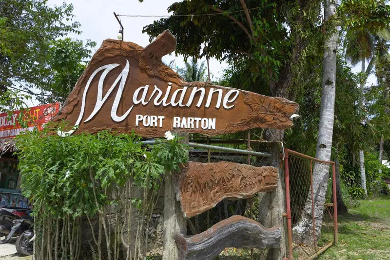 Panneau en bois sculpté avec le nom d'un lieu et une végétation luxuriante en arrière-plan.