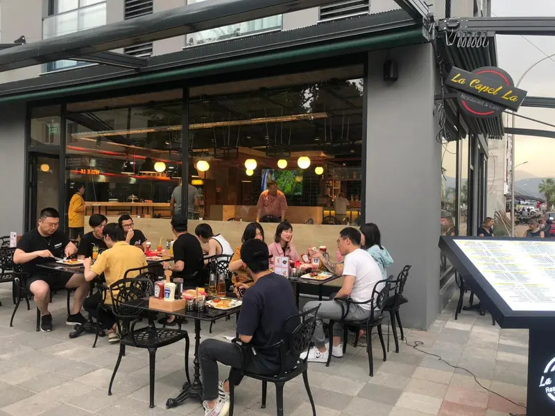 Terrasse de restaurant avec des clients attablés devant une grande baie vitrée.