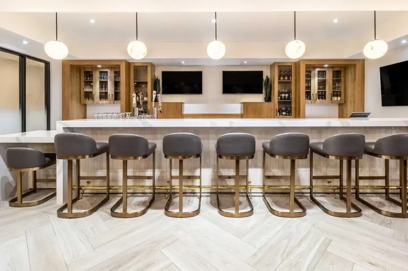 Un long comptoir de bar avec des tabourets est éclairé par des suspensions lumineuses.