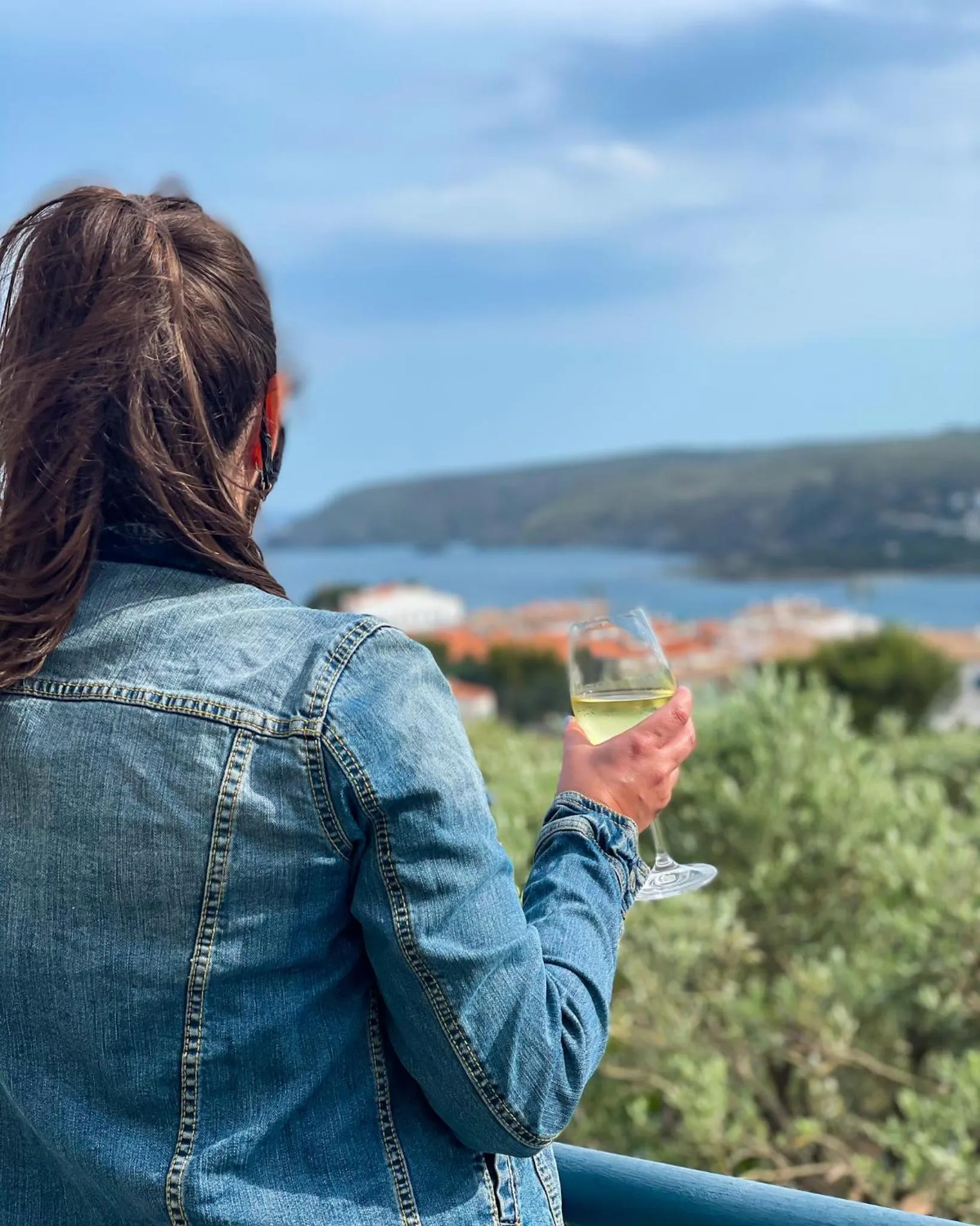 Une personne vue de dos tient un verre sur une terrasse ensoleillée.