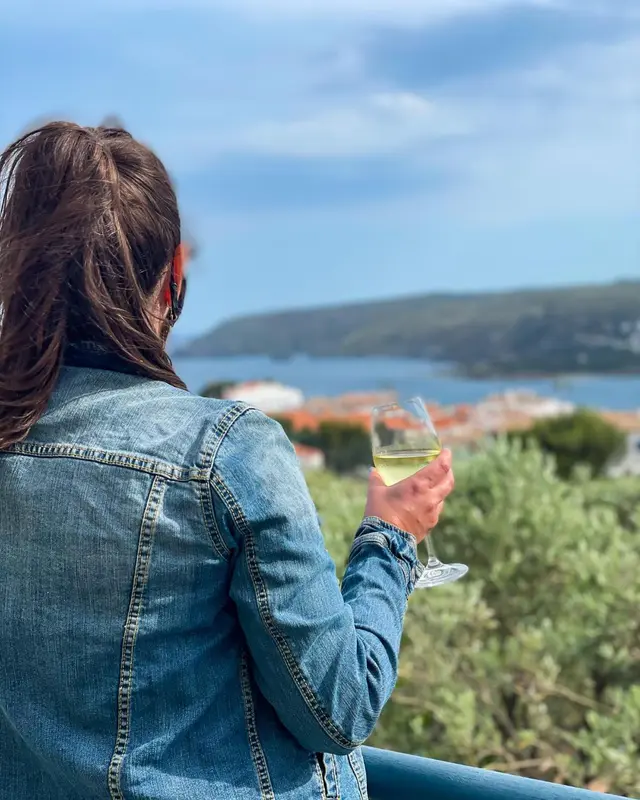 Une personne vue de dos tient un verre sur une terrasse ensoleillée.