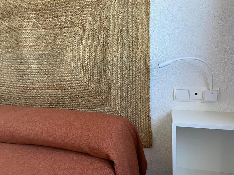 Un lit avec une tête de lit en fibres naturelles et une lampe murale.