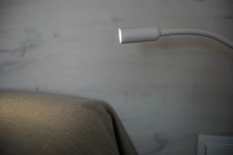 Une lampe orientable éclaire un coin de lit.