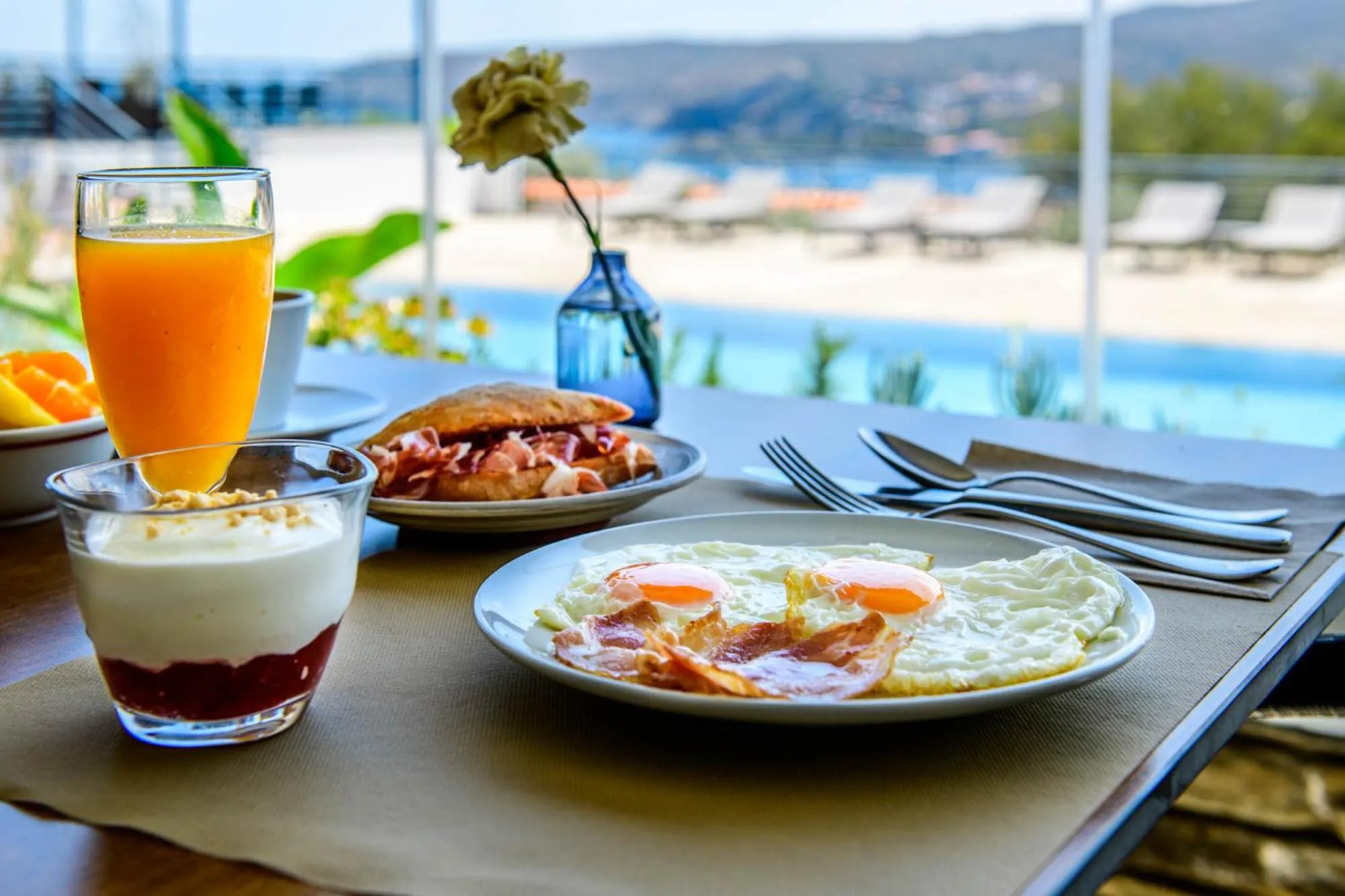 Un petit-déjeuner copieux est servi sur une table avec vue sur la mer et la piscine.