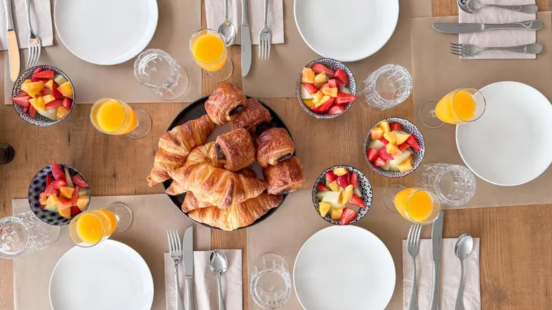 Une table dressée pour le petit-déjeuner avec des viennoiseries, des fruits et du jus d'orange.
