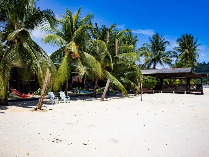 Plage de sable blanc bordée de palmiers et de quelques bungalows.