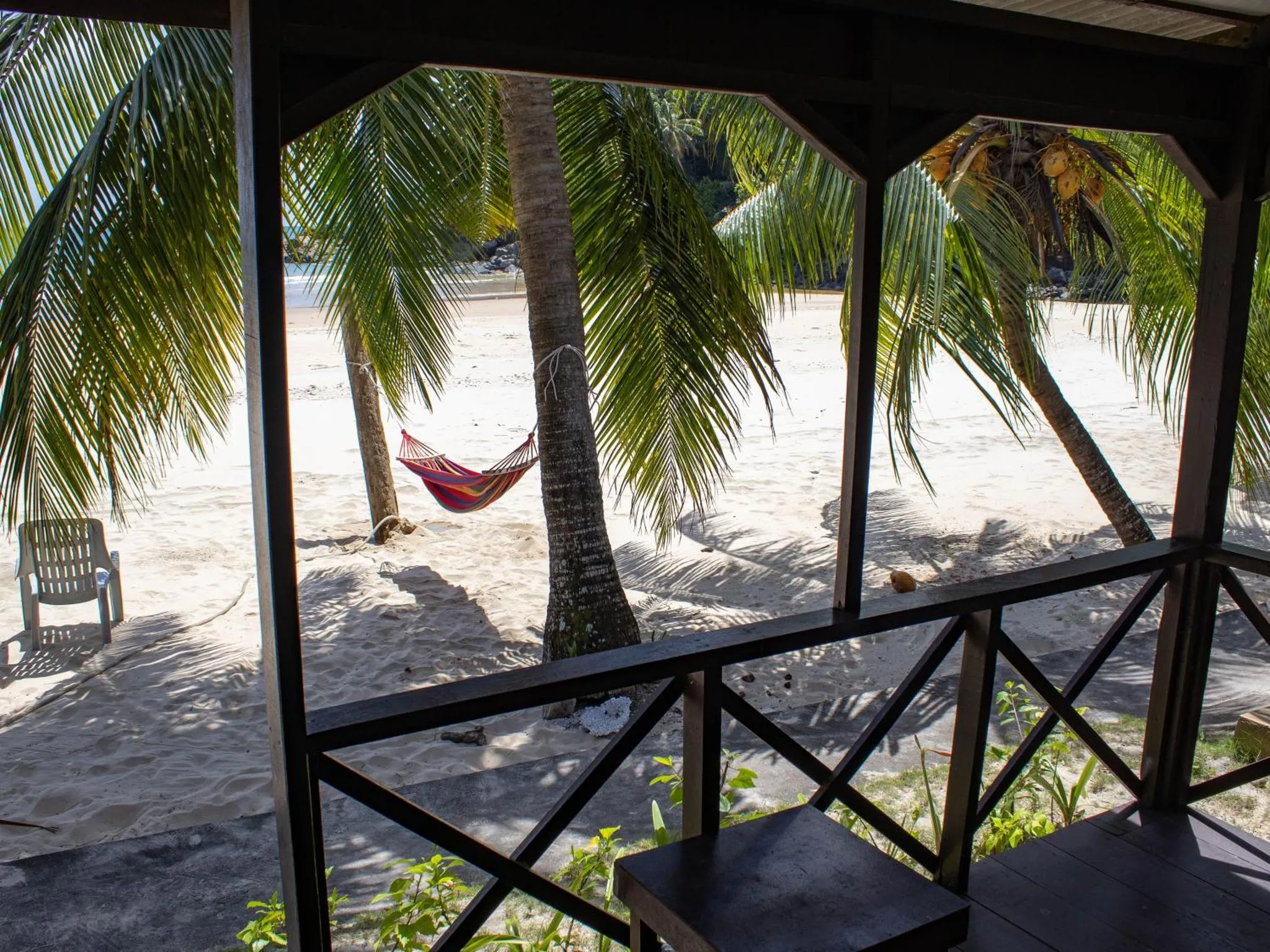 Une vue sur une plage de sable blanc bordée de palmiers depuis une terrasse ombragée.