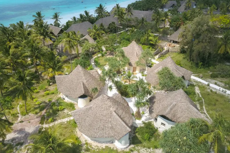 Vue aérienne d'un ensemble de bungalows aux toits de chaume bordant une plage de sable blanc.
