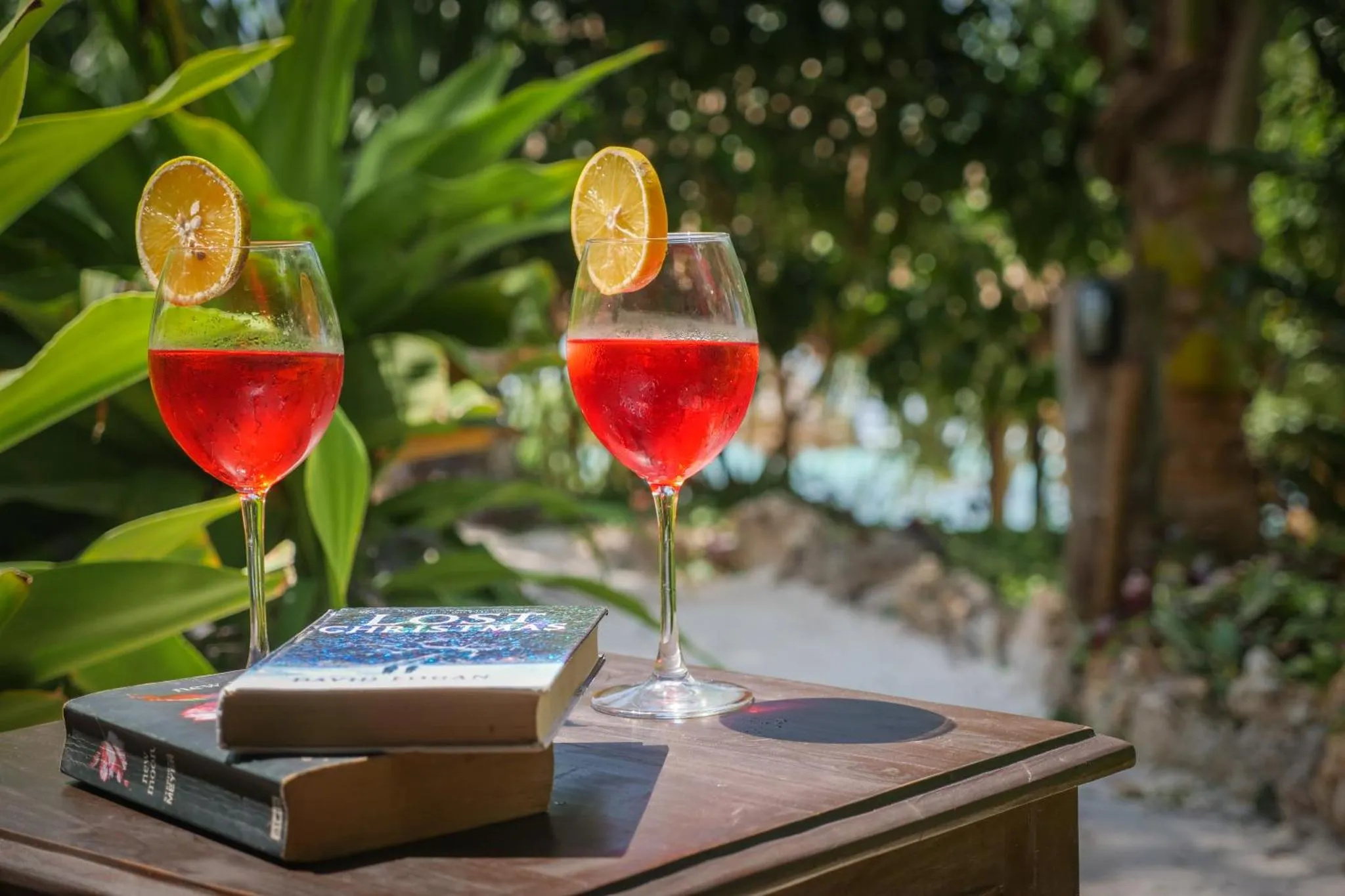 Deux verres de cocktail colorés reposent sur une table en bois avec un livre ouvert.
