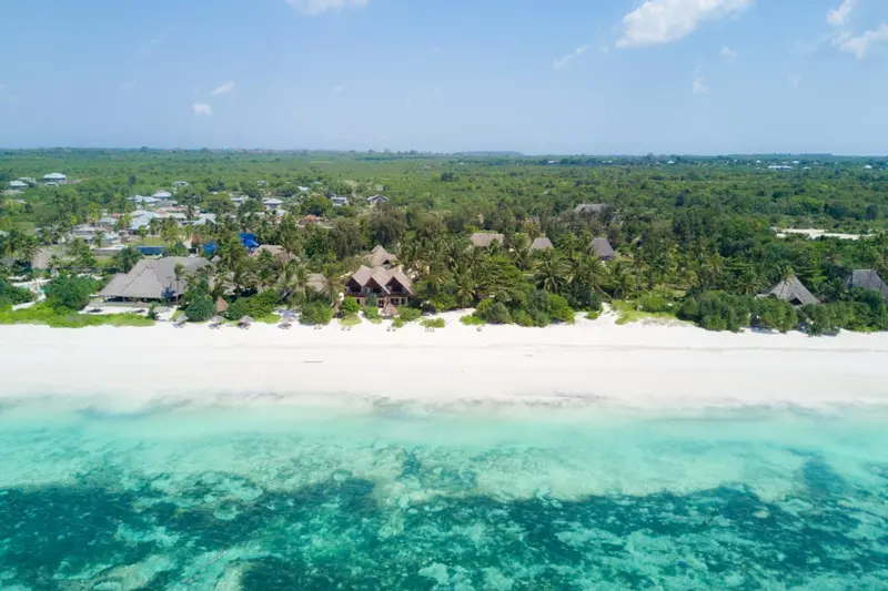 Vue aérienne d'une plage de sable blanc bordée de végétation luxuriante et de bungalows.