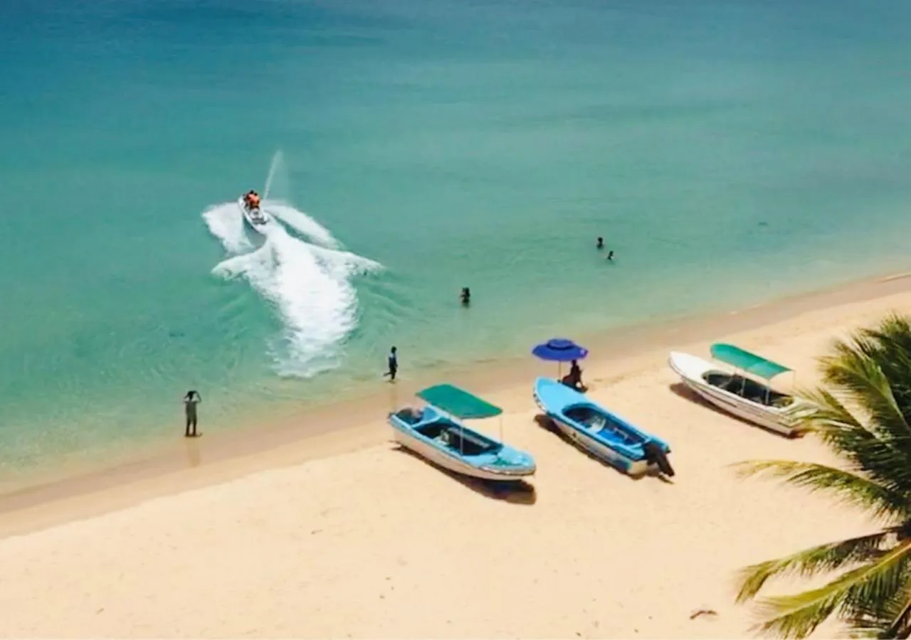 Une plage de sable clair avec des bateaux à moteur et des personnes sur le rivage.