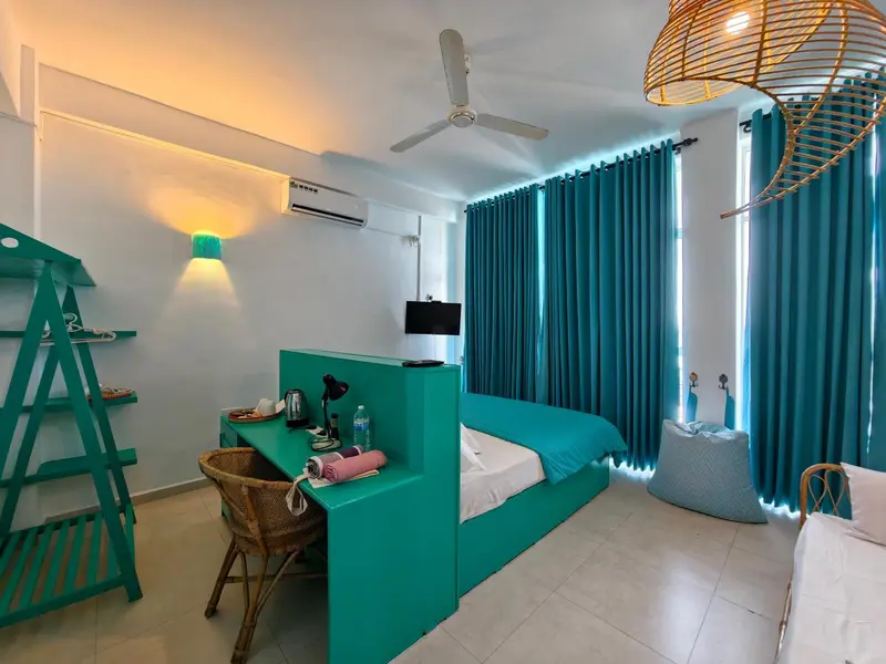 Une chambre lumineuse avec un lit turquoise et un bureau en bois.
