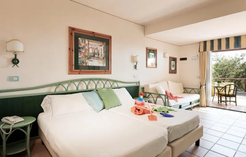 Une chambre lumineuse avec un lit double et un canapé face à une baie vitrée.