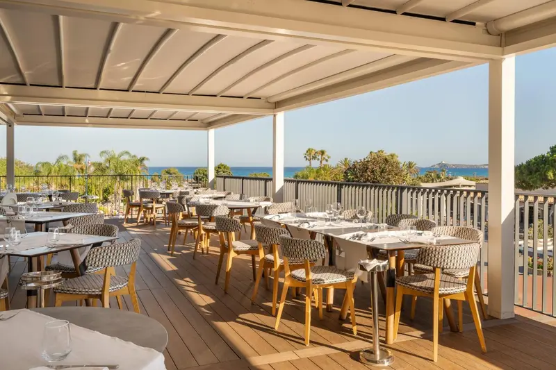 Terrasse ombragée avec tables et chaises donnant sur la mer.