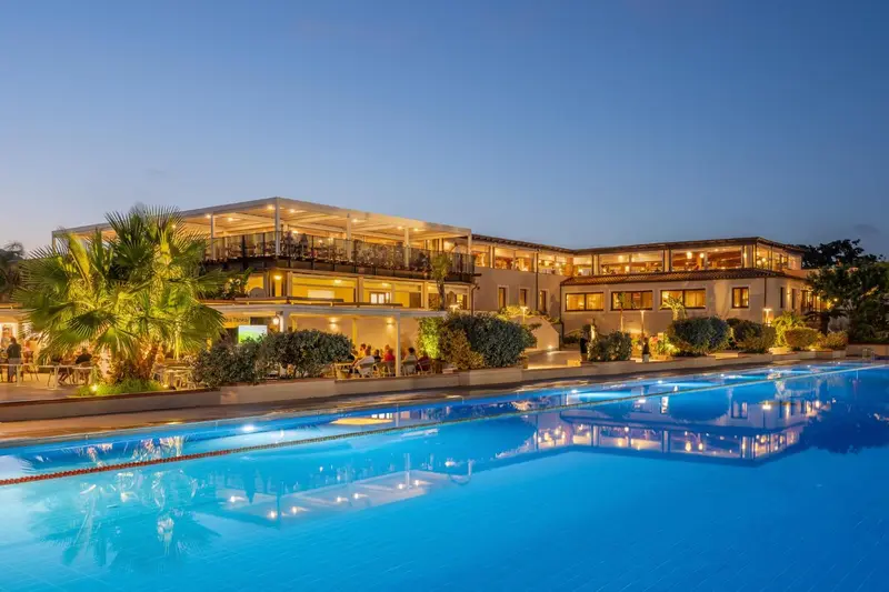 Bâtiment éclairé au bord d'une piscine la nuit.