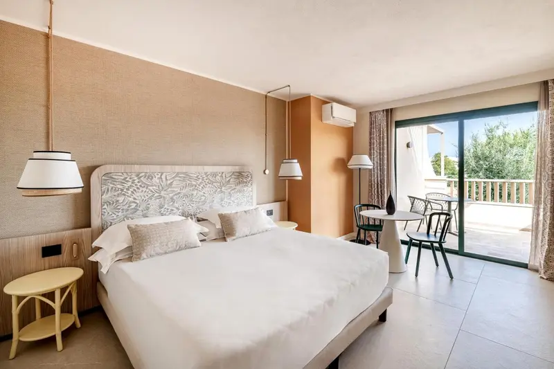 Une chambre lumineuse avec un grand lit et un coin salon donnant sur une terrasse.