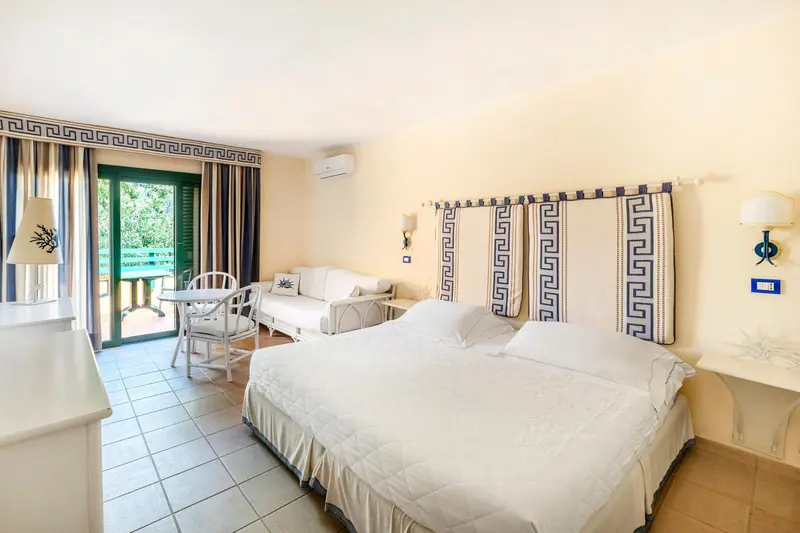 Chambre lumineuse avec un lit double et un canapé près d'une baie vitrée.
