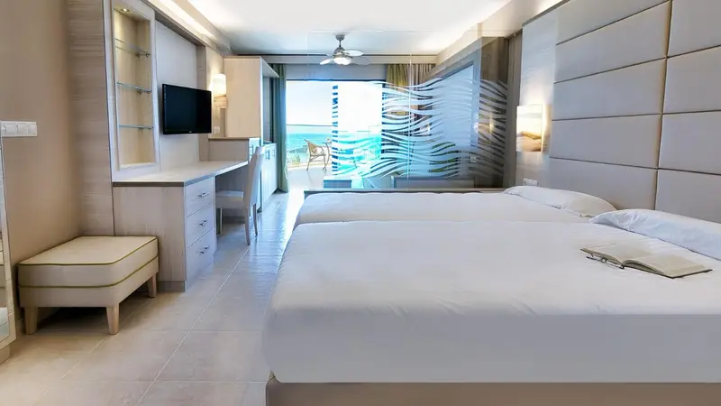 Chambre lumineuse avec deux lits et vue sur la mer.