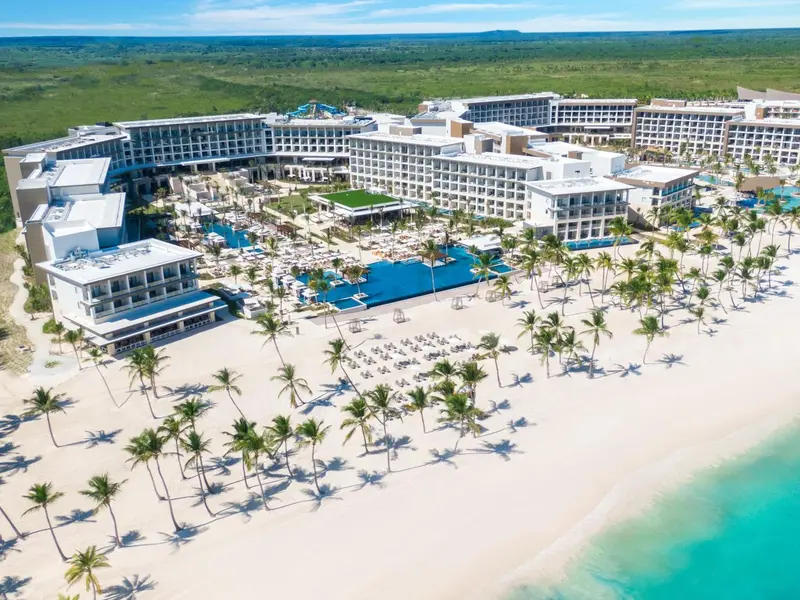 Vue aérienne d'un complexe hôtelier blanc avec des piscines et une plage de sable fin.