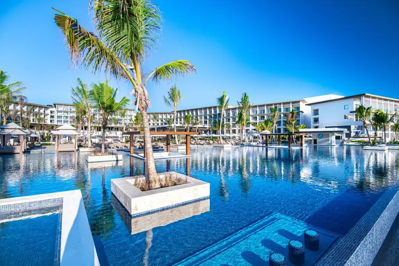Vue d'une piscine d'hôtel avec des palmiers et des transats.