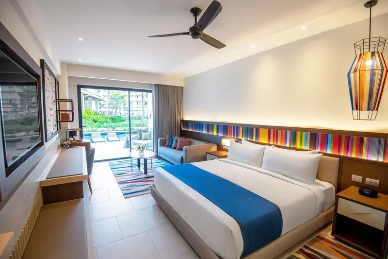 Une chambre lumineuse avec un grand lit et un canapé face à une baie vitrée.