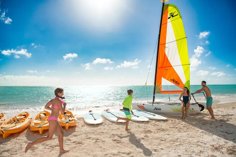 Une plage ensoleillée avec des activités nautiques et des personnes se promenant sur le sable.
