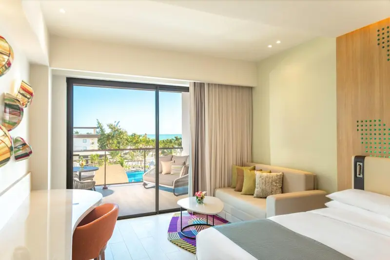 Une chambre lumineuse avec un coin salon et une vue sur la mer depuis un balcon.