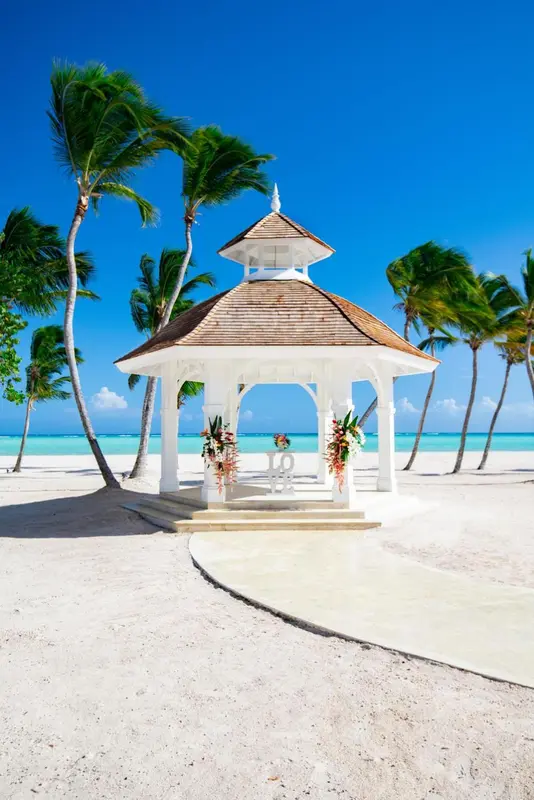 Un gazebo blanc orne une plage de sable fin sous des palmiers.