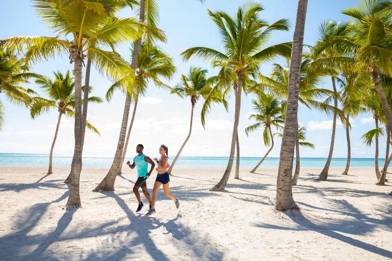 Deux personnes courent sur une plage de sable blanc bordée de palmiers.