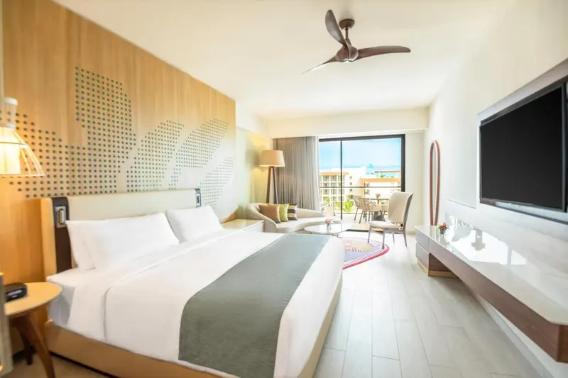 Chambre lumineuse avec un grand lit et un espace salon ouvert sur une terrasse.