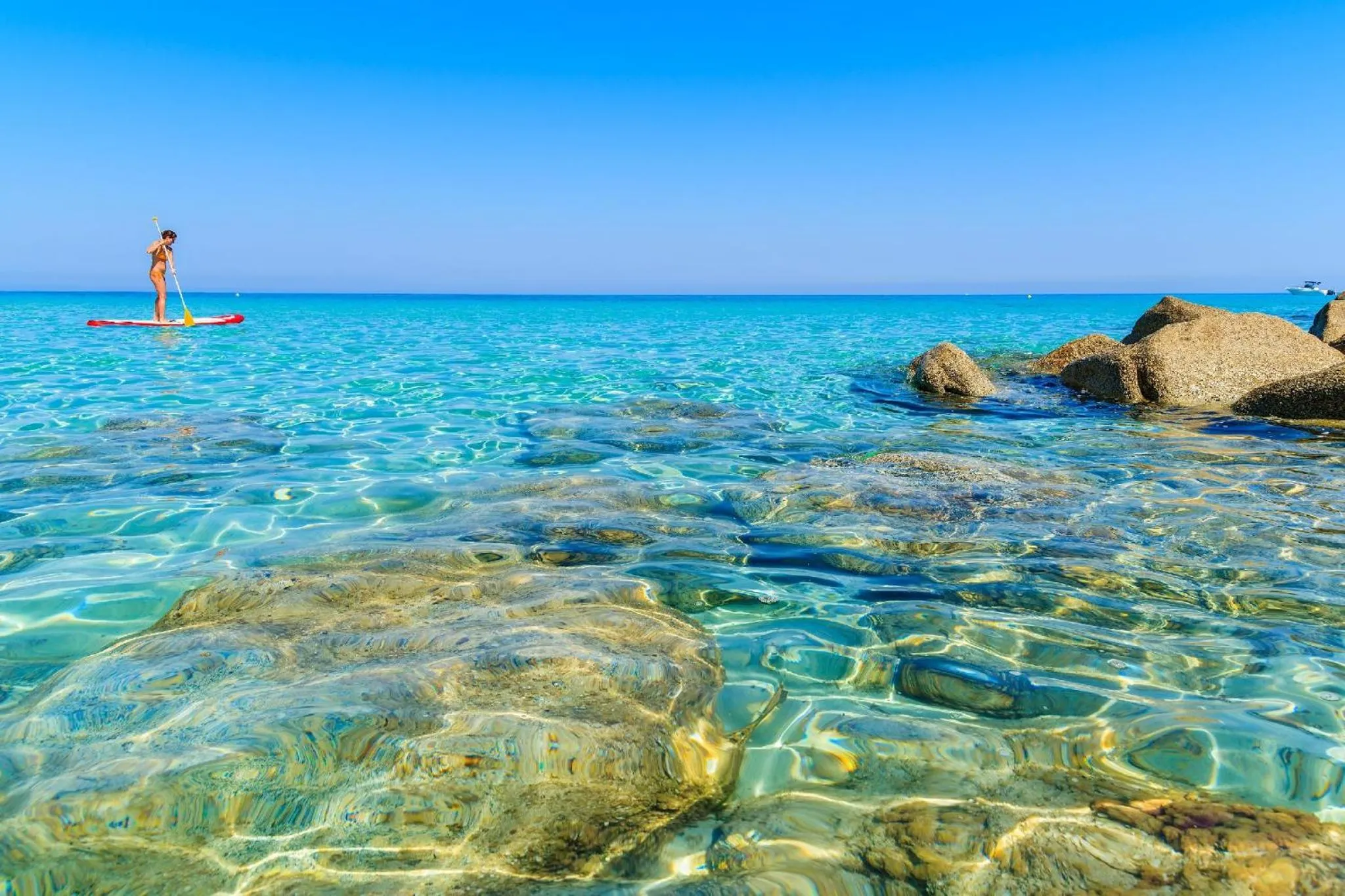 Une personne pratique le stand-up paddle sur une eau turquoise et claire.