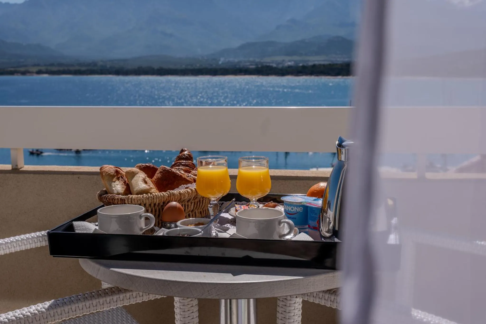Un plateau de petit-déjeuner est servi sur une table en osier avec vue sur la mer.