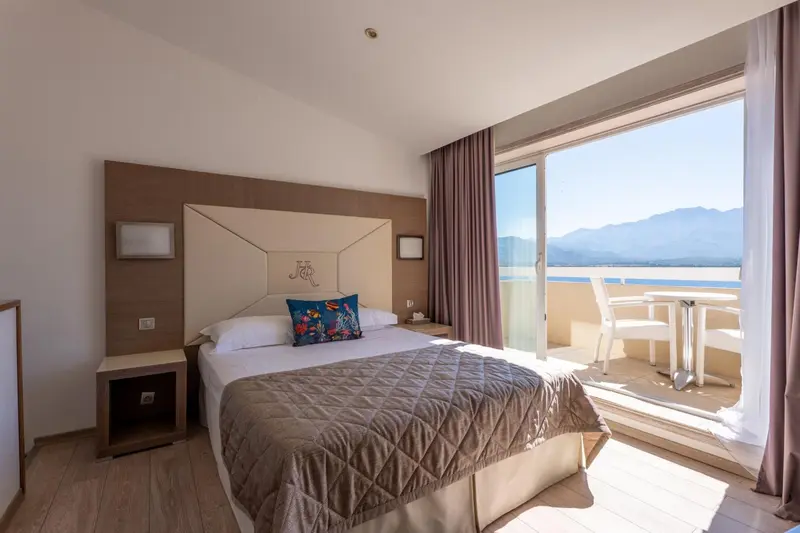 Chambre lumineuse avec un grand lit et une vue sur la mer depuis un balcon.