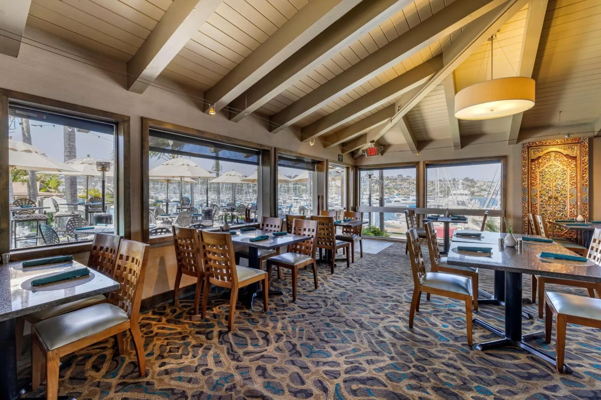Une salle de restaurant lumineuse avec de grandes fenêtres donnant sur un port de plaisance.