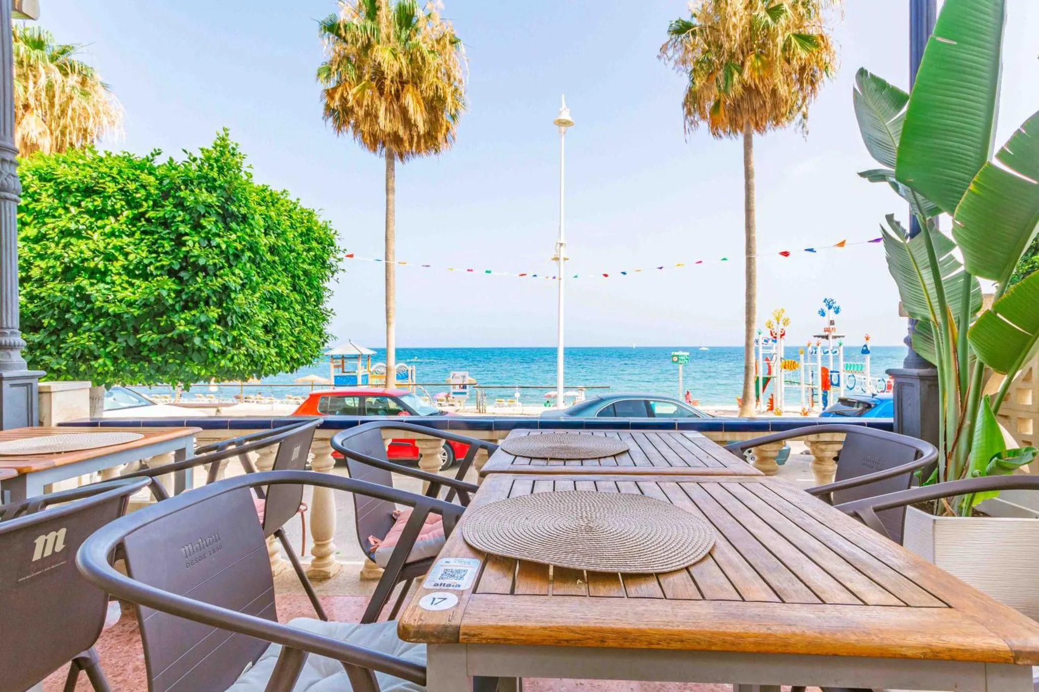 Tables en bois sur une terrasse ombragée avec vue sur la mer.